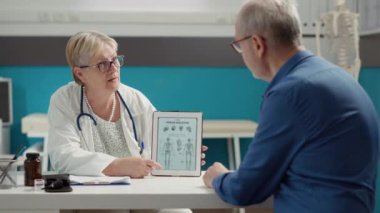 Tıbbi uzman dijital tabletteki insan iskeleti görüntüsünü açıklıyor, hastayla anatomi teşhisi hakkında konuşuyor. Ortopedik hastalık ve osteopati uzmanlığıyla kemik incelemesi.