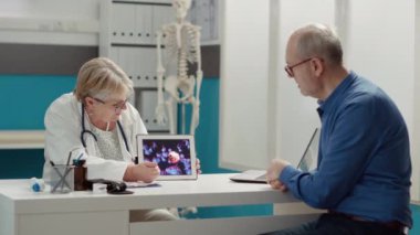 Koronavirüs animasyonlu dijital tablet tutan kadın doktor, sağlık kontrolündeki emeklilere salgın hastalıkları açıklıyor. Cihaz ekranında virüs çizimi, covid 19 önleme.