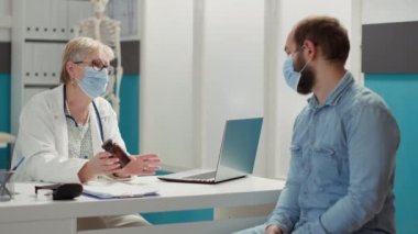 Kadın doktor, check-up 'ta hasta adama ilaç veriyor. Coronavirus salgını sırasında kabinede buluşuyor. Tedavi için ilaç, vitamin, ağrı kesici ve ilaç şişesinde..