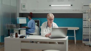 Hasta randevusunu planlamak için dizüstü bilgisayarla çalışan kadın sağlık uzmanının portresi. Genel pratisyen, teşhis ve tedaviye yardımcı olmak için ilaç notları kullanıyor.