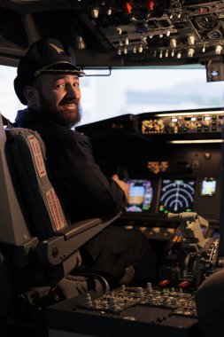 Jet kabininde panel komutuyla uçan gülümseyen erkek kaptan portresi, kontrol düğmesi ve ön camlı radar navigasyonu kullanarak uçak uçuruyor. Hava taşımacılığı.