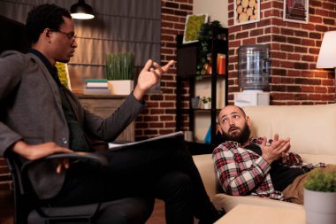 Psikolojik sorunlar hakkında erkek danışmanla konuşan beyaz bir adam terapi seansında kanepede uzanıyor. Terapistten tavsiye ve destek almak, psikanaliz yapmak..