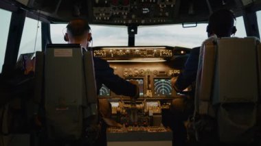 Kaptan ve yardımcı pilot, uluslararası havayolu uçağıyla havalanmak için uçak kulpu kullanıyor. Gösterge panelinde kontrol paneli komutu kullanılıyor ve kokpitte yön değiştiriliyor. El kamerasıyla..
