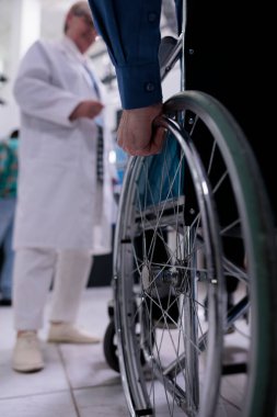 Özel hastane resepsiyonunda randevu için yaşlı adamın doktor önünde tekerlekli sandalye kullanması. Klinikte engelli olarak yaşayan yaşlı adama odaklanın..
