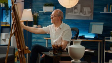 Yaşlı sanatçı tuval üzerine profesyonel bir başyapıt çizmek için kalemler kullanıyor, araçlarla sanat tasarımı ve çizim yapıyor. Sanatsal becerileri ve otantik tasarım modeli, sanat ve zanaat içeren vazo çizimi.