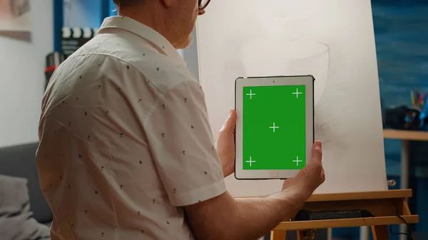 Old man using digital tablet with greenscreen background and drawing sketch masterpiece with artistic tools. Holding phone with blank chroma key template, isolated mockup copyspace.