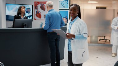 Hastanenin resepsiyon lobisindeki Afrikalı Amerikalı doktorun portresi. Muayene için hasta kabinesine götürme randevusuyla birlikte check up dosyalarını analiz ediyor. Sağlık uzmanlığı olan bir doktor..