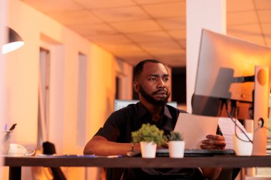 İdari Müdür evrak raporlarını analiz ediyor ve büyük pencereli araştırma sunumu yaratmak için notlar alıyor. Gün batımında belge ve bilgisayarla proje verileri üzerinde çalışmak.