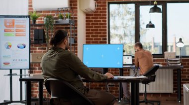 İzole edilmiş yeşil ekranı inceleyen serbest çalışan bir erkek, başlangıç ofisinde çalışıyor. Bilgisayar görüntüleme uygulamasında boş krom anahtar şablonu kullanılıyor.