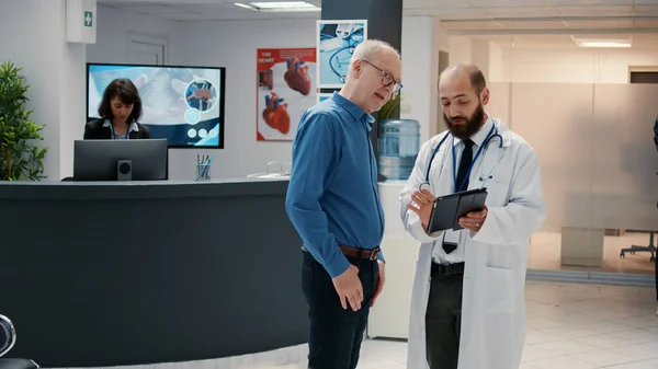 医生和老年患者在医院接待处看数码平板电脑 谈论候诊区的医疗诊断 与专家进行预约检查 以提供意见 — 图库照片