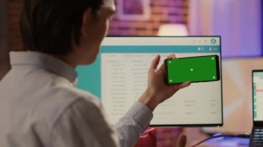 Office worker looking at horizontal greenscreen on smartphone, using blank chroma key with mockup copyspace template and isolated background. Mobile phone application on display.