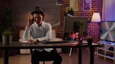 Asyalı serbest çalışan telefonda konuşuyor. Bilgisayarda finans işi yapmak için. Yöneticiyle konuşmak için akıllı telefon hattını kullanıyor. Evrak işleri için cep telefonu görüşmesi. El kamerasıyla..