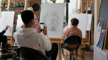 Sanat dersinde akıllı telefondan vazonun resmini çeken yaratıcı bir öğrenci. Genç adam fotoğraf çekmek için cep telefonu kullanıyor ve eğitim dersinde çizim tekniğini hatırlıyor..