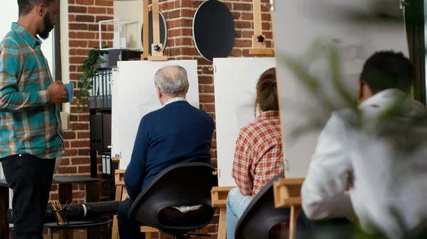 Young person talking to elder man about vase drawing, teaching artistic skills in educational workshop. Attending art class program to learn to draw artwork on canvas, creative practice.