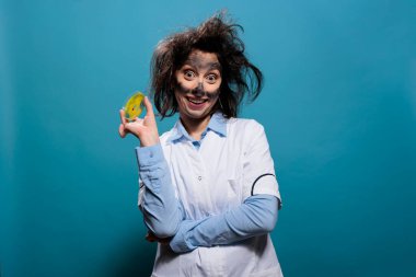 Çılgın kimyagerin zehirli biyolojik atık maddesiyle dolu bir petri kabı var ve kameraya berbat gülümsüyor. Elinde cam levha örneğiyle ürkünç sırıtan çılgın bilim adamı.