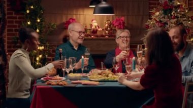 Happy close family members clinking champagne glasses while sitting together at Christmas dinner table. Joyful multiethnic group of people celebrating winter holiday with sparkling wine.