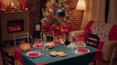 Interior of traditional and authentic season cozy setting celebrating religious event. Empty festive christmas dinner table inside decorated living room with holiday garlands and dinnerware.