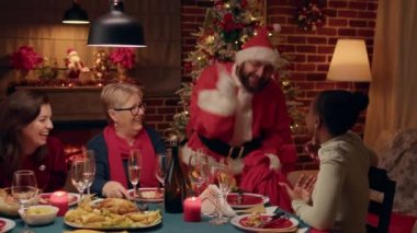 Evdeki Noel yemeğinde Noel Baba kılığına girmiş bir adam mutlu bir kadınla konuşuyor. Neşeli Afrikalı Amerikalı kadın kış tatilini kutlarken kocasının Noel Baba gibi görünmesine şaşırdı..