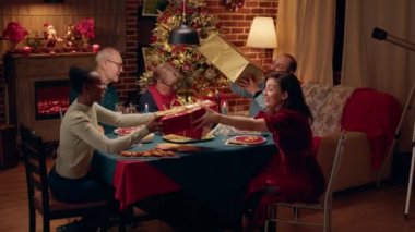 Multiethnic family members celebrating traditional winter holiday while giving each other presents. Joyful people gathered at Christmas dinner table while exchanging gifts.