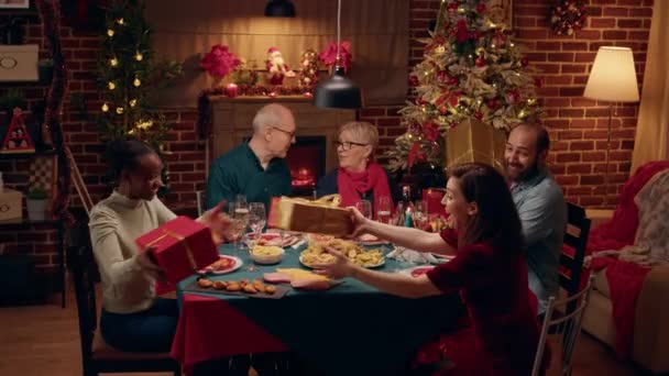Радісні Люди Збиралися Різдвяним Столом Обмінюючись Подарунками Мультинаціональні Сім Святкують — стокове відео