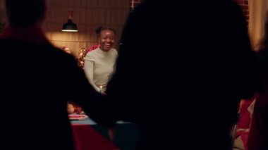 Joyful interracial couple welcoming guests to Christmas dinner at home. Festive people gathering in dining room to celebrate winter holiday with traditional home cooked food.