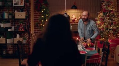 Interracial couple welcoming senior people and young woman at Christmas family dinner table. Festive people gathering at home to celebrate winter holiday while giving each other gifts.