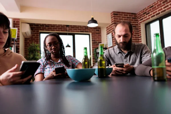 Kültürel çeşitlilikte insanlar oturma odasında otururken modern akıllı telefon cihazlarıyla internete göz atıyorlar. Cep telefonlarında çevrimiçi video içeriği izlerken evde oturan çok ırklı arkadaşlar.