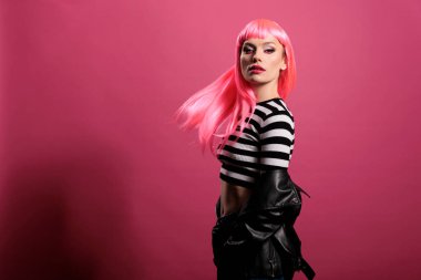 Portrait of confident person looking at camera in studio, posing with natural leather jacket and pink hair. Attractive woman with punk rocker fashion style feeling carefree and sensual.