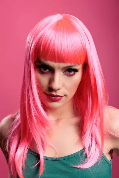 Portrait of fashion model with pink hair wig and stylish makeup posing in studio over background. Sexy carefree woman feeling attractive and beautiful in front of camera, fun glamour.