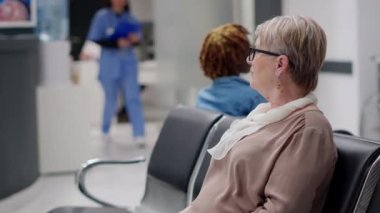 Bekleme salonunda bekleyen yaşlı bir kadın tıbbi randevuya katılmak için tesiste uzman doktorla muayene oluyor. Hastanenin resepsiyonunda bekleyen kadın hasta..