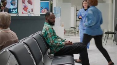 Male patient waiting in hospital reception lobby to attend medical checkup with doctor at healthcare clinic. Asian assistant and man doing consultation examination with physician at facility.