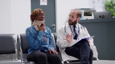 Servikal boyun köpüğü olan kadın hasta, sağlık merkezinin bekleme salonunda doktorla konuşuyor. Boyunluk takmış yaralı bir kadın fiziksel yaraları tedavi etmeye çalışıyor. Sağlık görevlilerinden yardım almaya çalışıyor. El kamerasıyla..