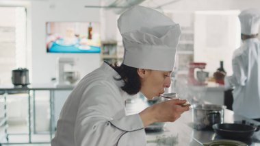 Kadın aşçı fırında sıvı sos tadıyor mutfak yemeği yapmak için, mutfak tarifini taze malzemelerle pişiriyor. Üniformalı bir kadın profesyonel menü yaratmak için restoran mutfağında çalışıyor. Kapat..