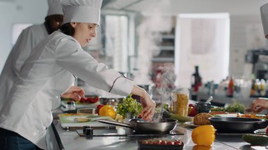 Kadın aşçı, tavada profesyonel aşçılık yapıyor. Lezzetli yemekler yapmak için yemek tarifi kullanıyor. Şef lokanta mutfağında gastronomi yemekleri pişiriyor, malzemeleri hazırlıyor. El kamerasıyla..