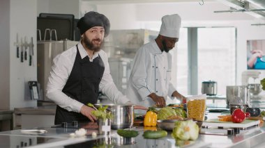 Erkek aşçı POV kamera önünde yemek tarifini açıklayan bir video kaydı yapıyor. Profesyonel mutfakta gastronomi programı için üniformalı genç aşçı. Üçayak atışı.
