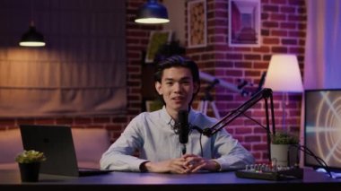 Asian vlogger filming podcast show talking to internet audience, recording vlog to create social media content. Live broadcast episode to chat with listeners, studio production. Tripod shot.