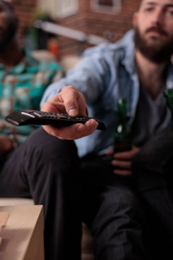 Genç insan TV 'yi uzaktan kumandayla kanal ya da televizyon programlarını değiştirip toplanan bir grup insanla film izlemek için kullanıyor. Eğlence aktivitesi için film ya da televizyon programı aranıyor. Kapat..