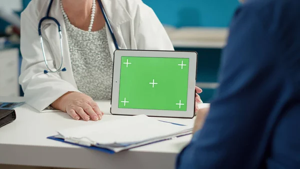 Health specialist holding horizontal greenscreen on digital tablet, at checkup with patient. Mockup blank template with isolated chroma key background and copyspace on display. Close up.