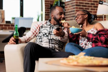 Mutlu kız arkadaş ve erkek arkadaş TV 'de abur cuburla ve filmle eğleniyor uzaktan kumandayla kanal değiştiriyor. Cips yemek, paket servis yemeği yemek, televizyonda film izlemek..