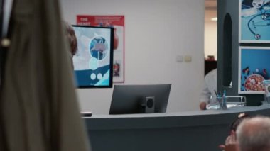 Hastane çalışanı resepsiyonda çalışıyor. Bekleme odasındaki doktor ve hastalara idari bilgiler veriyor. Tıbbi klinik lobisi ve yardım sayacı.