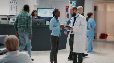Erkek doktor, Afro-Amerikan bir hastayla sağlık hizmetleri hakkında konuşuyor. Hastane resepsiyonundaki bekleme odasındaki dijital tablette tıbbi teşhis sonuçlarını gösteriyor. Tesise sağlık ziyareti.