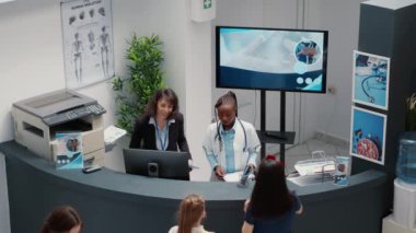 Yoğun hastane resepsiyonunda çalışan sekreter hastalara muayene için bekleme odasında yardım ediyor. Resepsiyonist, klinik lobisindeki bir grup insana tıbbi raporlar veriyor. El kamerasıyla..