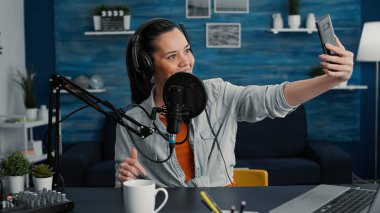 Yaratıcı içerik yaratıcısı podcast şovunu kaydederken özçekim fotoğrafı çekiyor. Ünlü internet yıldızı akıllı telefonuyla fotoğraf çekerken hem film çekiyor hem de izleyicilerle konuşuyor..