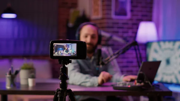 Selective focus on digital video camera screen recording influencer caucasian man streaming live talk show using microphone from home studio. Male content creator filming vlog for social media post.