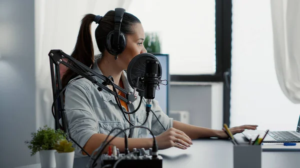 Creative podcaster hosting internet live talk show while sitting in studio. Popular influencer discussing last news with audience while wearing headphones and using professional microphone.