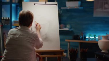 Female artist in retirement age using pencils to draw vase artwork on canvas, creating professional masterpiece with artistic skills. Drawing authentic sketch model with art and craft tools.