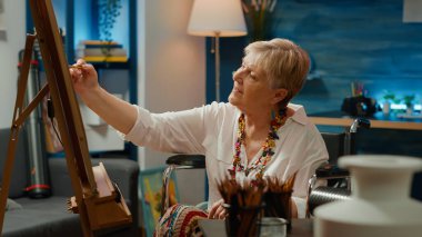 Fiziksel engelli, kötürüm bir kadın sanat ve zanaat hobisi için vazo modeli çiziyor. Tekerlekli sandalye kullanıcısı yaratıcılık becerilerini kullanarak sanat eseri tasarımı çiziyor.