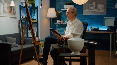 Yaratıcılık ve sanatsal araçlarla ilham aramak için dijital tablet kullanan emekli bir yetişkin. Beyaz tuval üzerinde otantik sanat eskizi oluşturuluyor, modern sanat şaheserleri çiziliyor.