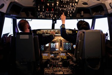Kaptan ve kadın yardımcı pilot kokpit komutasındaki gösterge paneliyle uçmaya hazırlanıyor. Uçak mürettebatı irtifa seviyesini düzeltiyor ve kontrol paneli düğmeleri ile uçuyor..