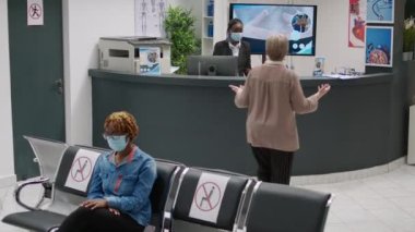 Busy hospital reception with diverse group of people during covid 19 epidemic, waiting to attend checkup appointment with specialist. Waiting room area during coronavirus pandemic.